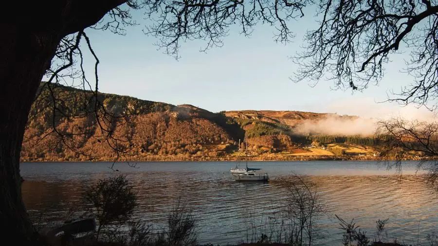 Loch with two sail boats on the water and a mountain on the other side