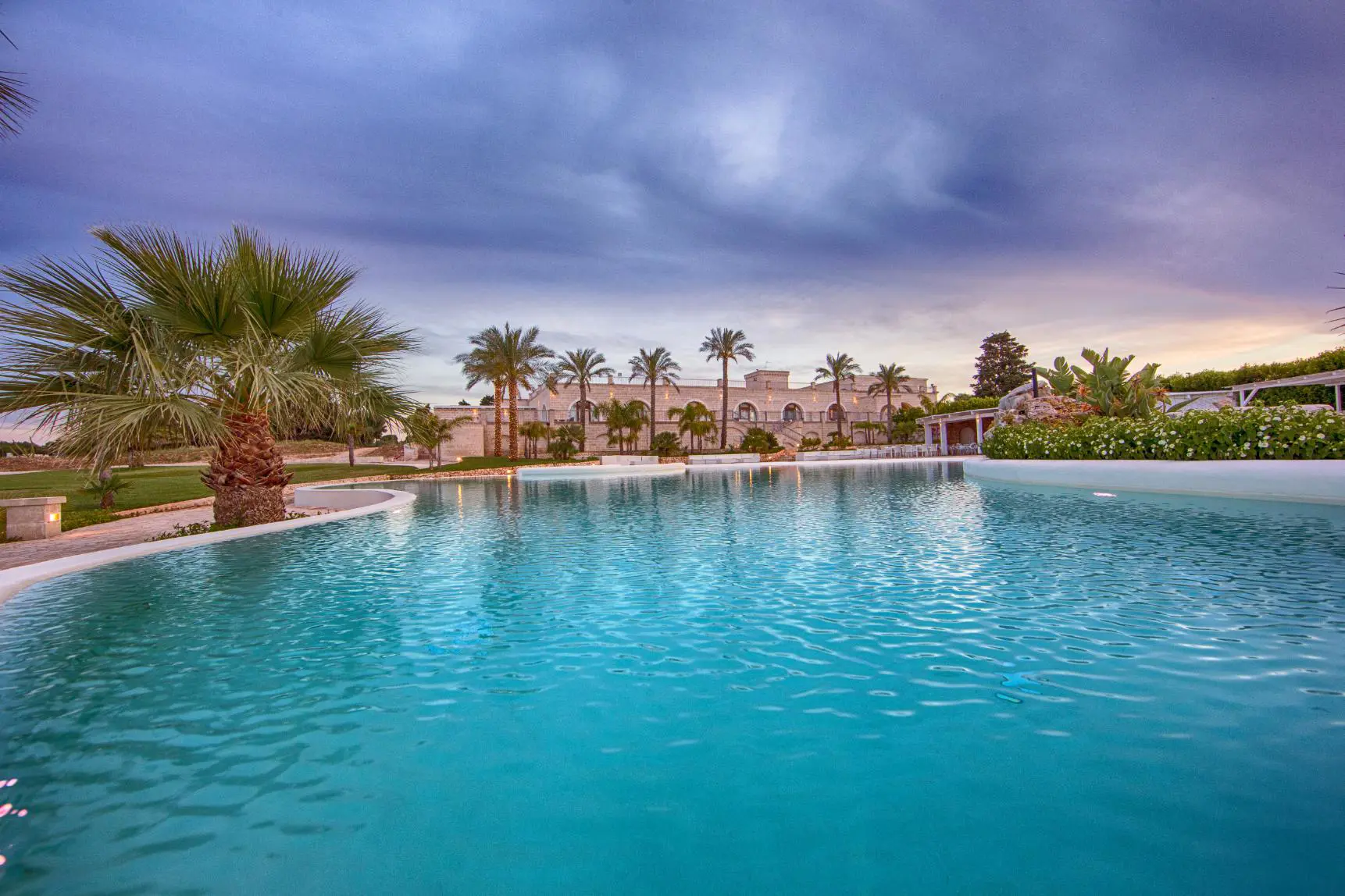 Scenic view of the outdoor pool at Masseria Caselli Hotel, Italy, surrounded by palm trees and gardens at sunset