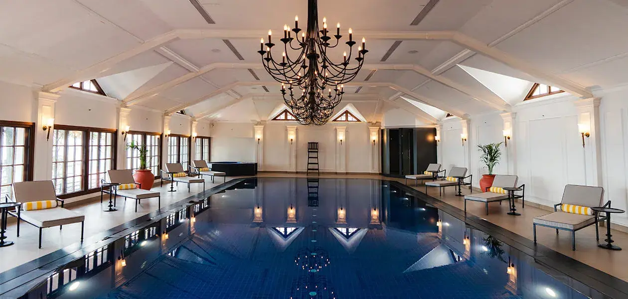 The Oberoi Cecil’s indoor swimming pool in Shimla, featuring a central black chandelier and modern sun loungers lining both sides of the pool