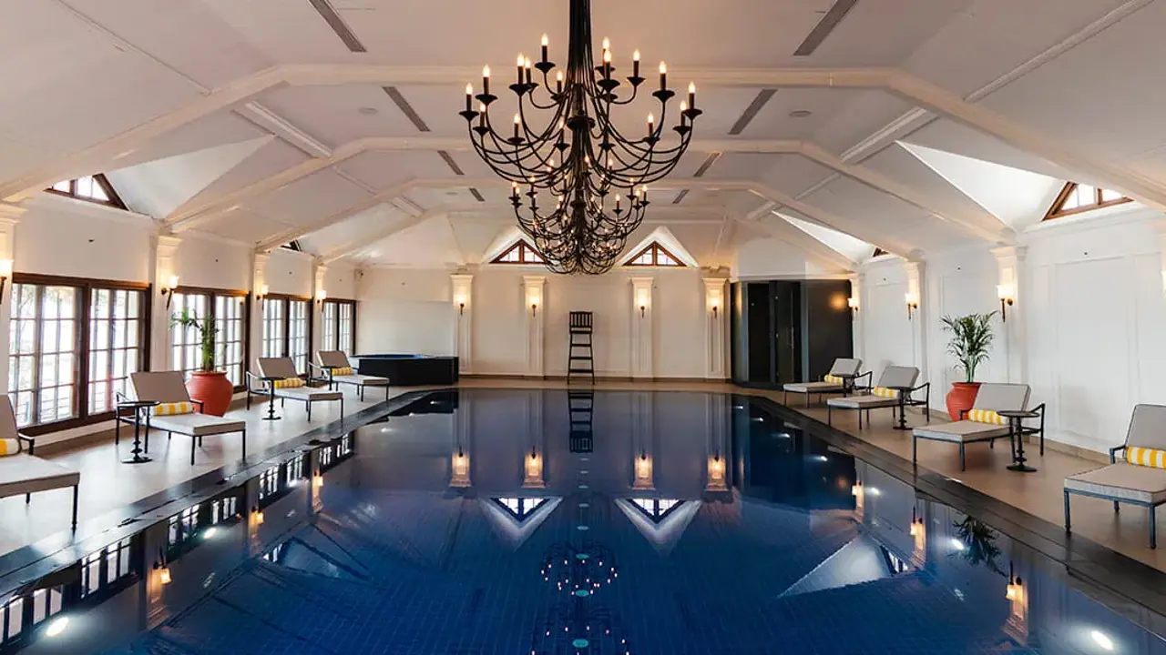 The Oberoi Cecil’s indoor swimming pool in Shimla, featuring a central black chandelier and modern sun loungers lining both sides of the pool