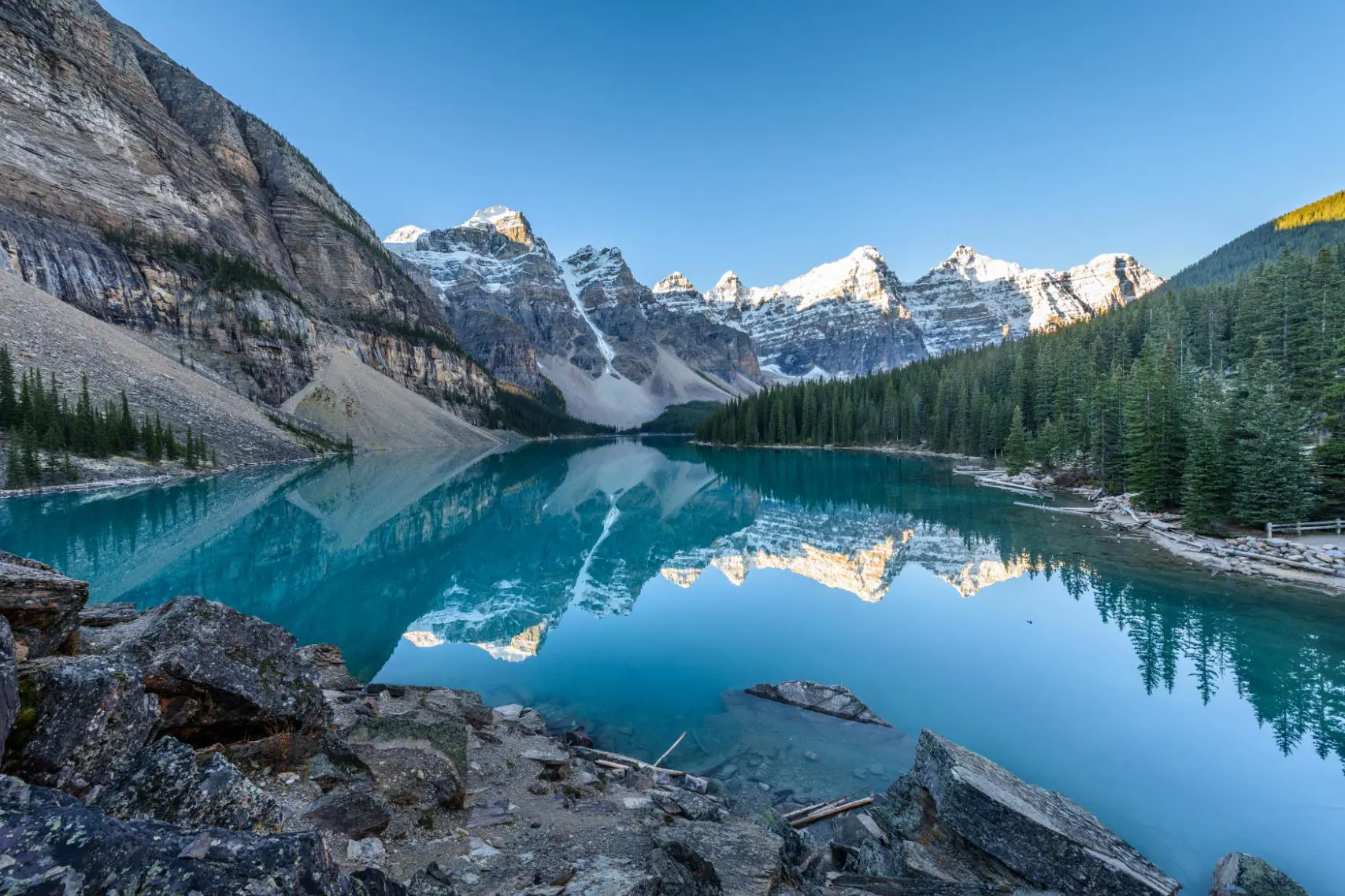 Moraine Lake in Banff National Park, with its striking turquoise water reflecting surrounding mountain peaks under sunny blue skies