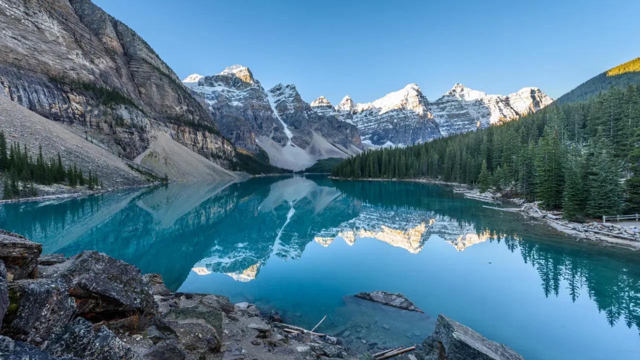 Moraine Lake in Banff National Park, with its striking turquoise water reflecting surrounding mountain peaks under sunny blue skies