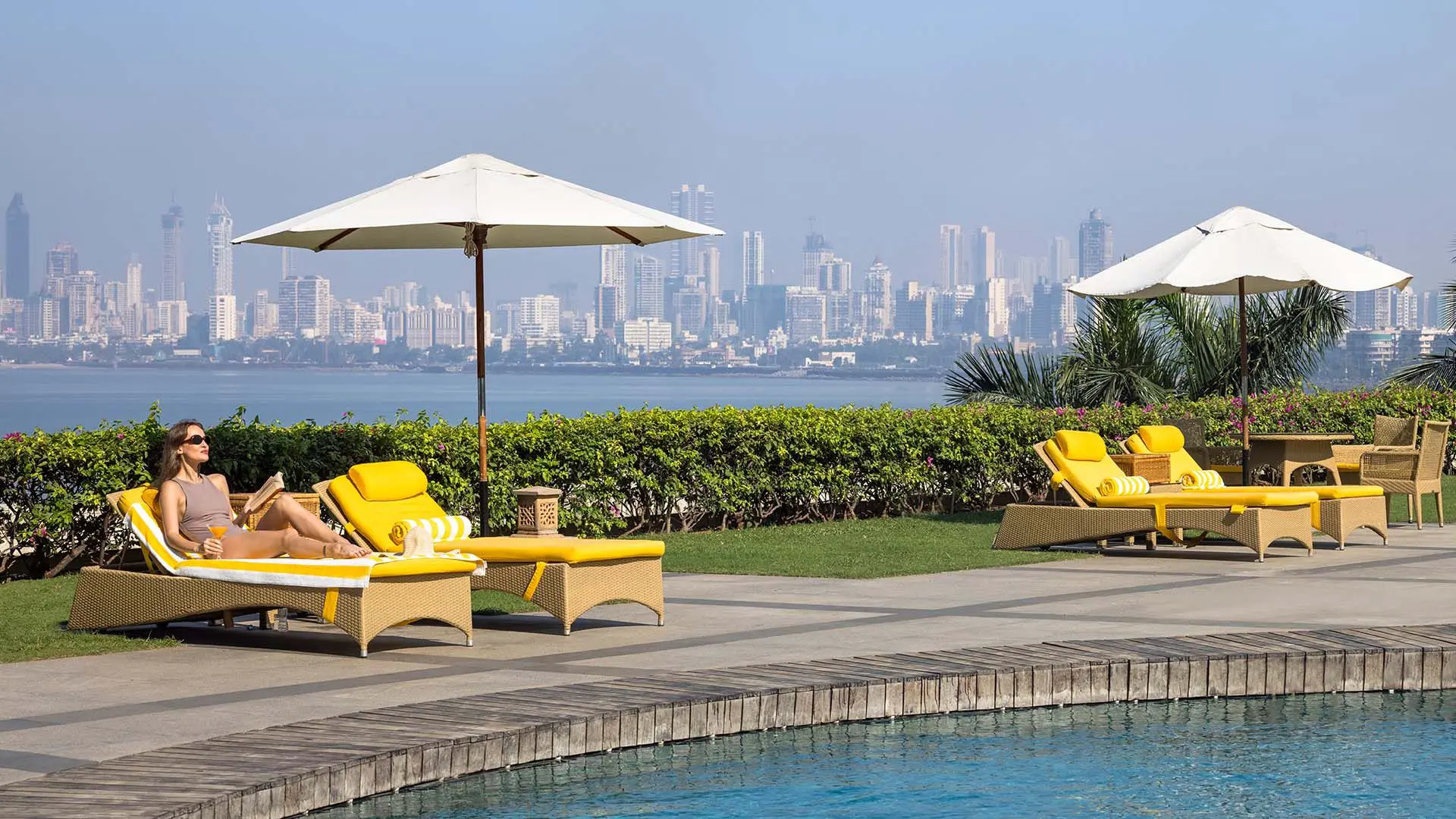 Outdoor swimming pool at Trident Nariman Point, Mumbai, with yellow sun loungers along the poolside and the city skyline in the background