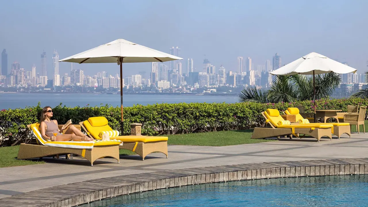 Outdoor swimming pool at Trident Nariman Point, Mumbai, with yellow sun loungers along the poolside and the city skyline in the background