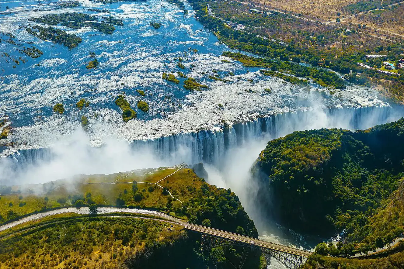 Aerial view of Victoria Falls in Zimbabwe, with water cascading over the cliffs and mist rising above the surrounding landscape