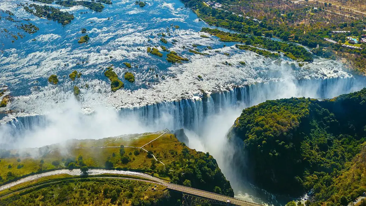 Aerial view of Victoria Falls in Zimbabwe, with water cascading over the cliffs and mist rising above the surrounding landscape