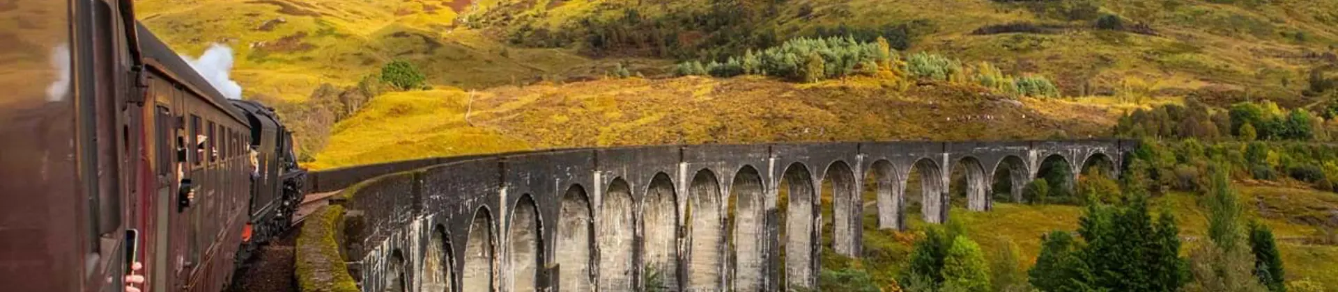 Shot of a steam train going along railway on a viaduct in the highlands from behind 