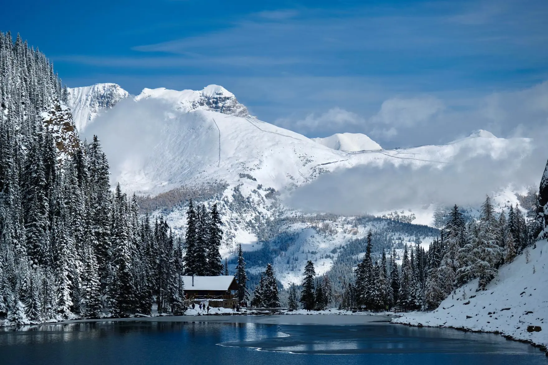 The Tea House at Lake Agnes nestled in snow-covered mountains beside a blue alpine lake