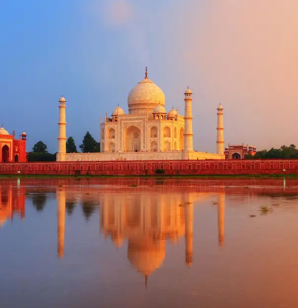 The Taj Mahal in Agra reflected in the calm waters of the Yamuna River at sunset