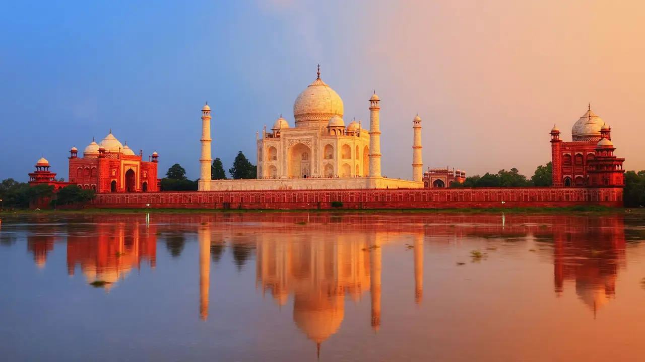 The Taj Mahal in Agra reflected in the calm waters of the Yamuna River at sunset