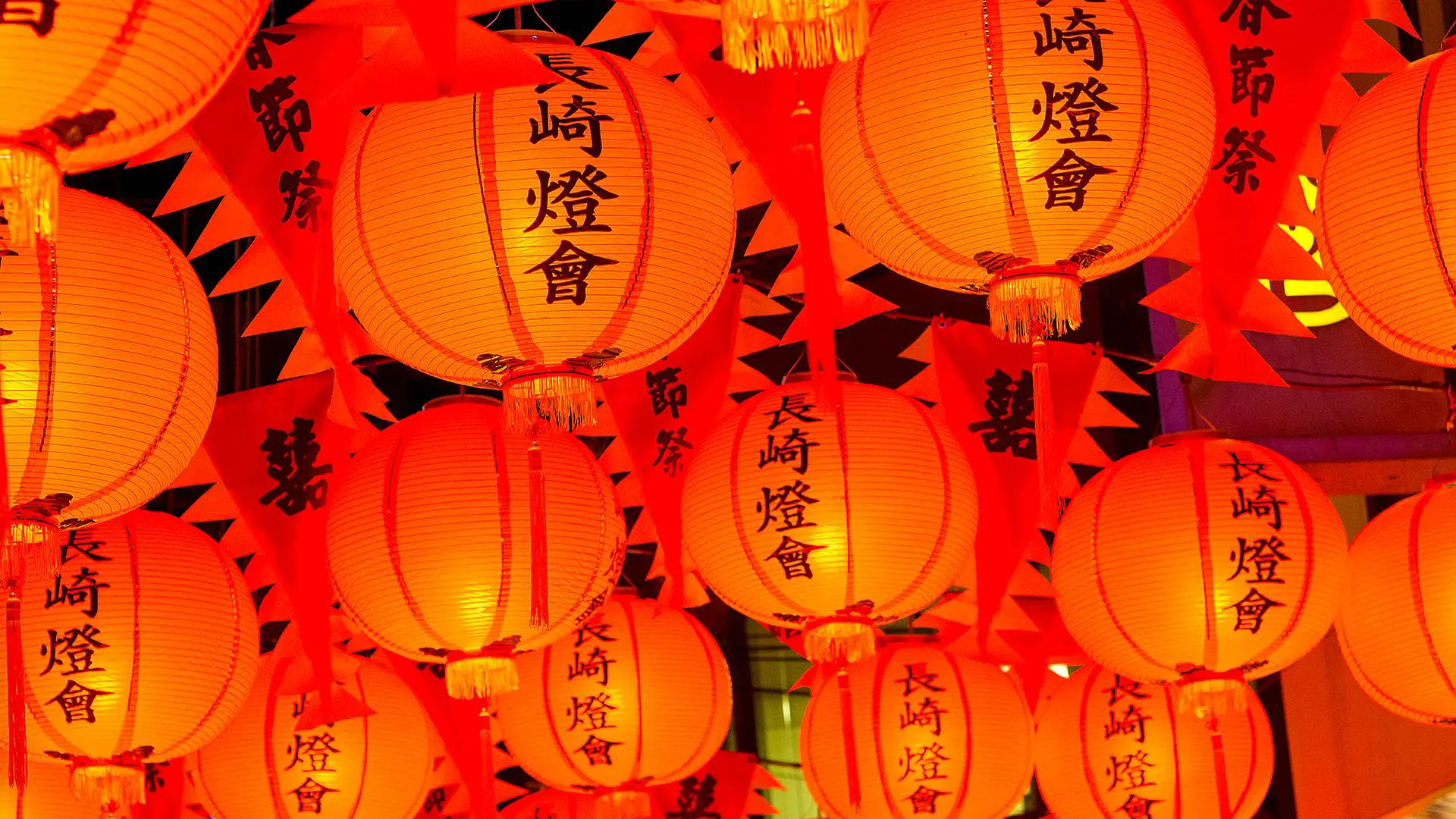 Bright orange-red paper lanterns with Japanese characters hanging overhead during a traditional festival in Kyushu, Japan