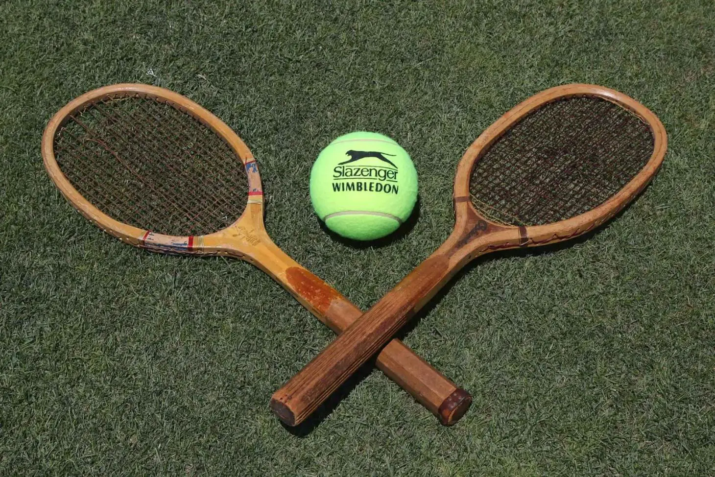 Two wooden tennis rackets and a yellow Slazenger tennis ball arranged on a green lawn