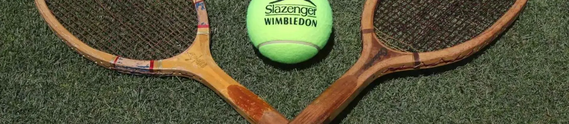 Two wooden tennis rackets and a yellow Slazenger tennis ball arranged on a green lawn