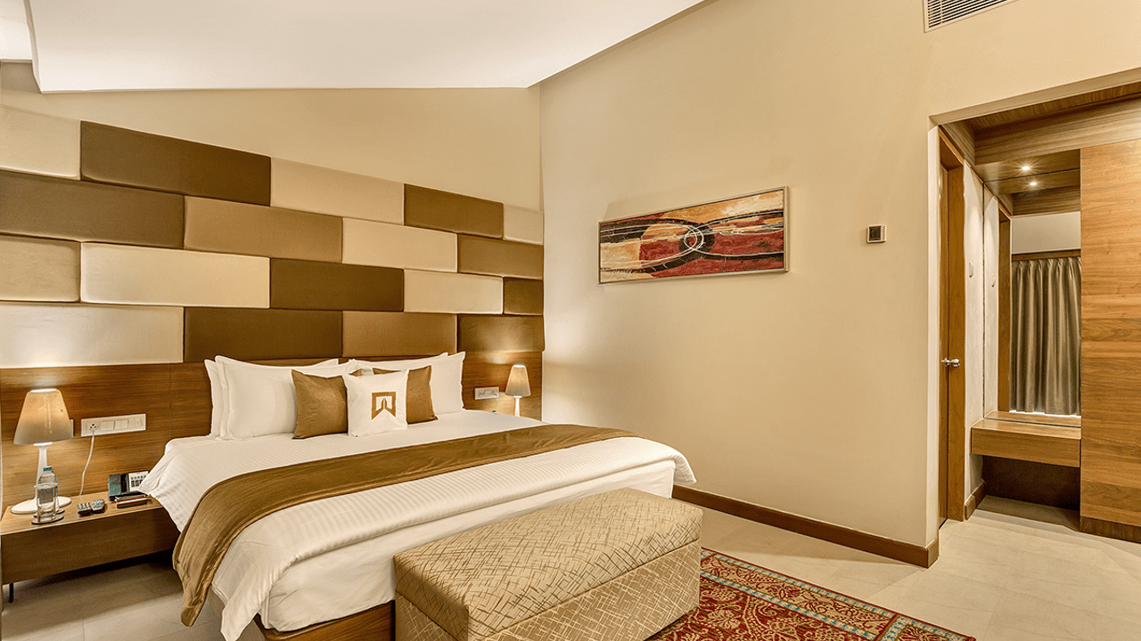 Spacious deluxe guestroom at Welcomhotel by ITC Hotels in Mahabalipuram, decorated in warm golden and neutral patterns, with a large double bed centred in the room