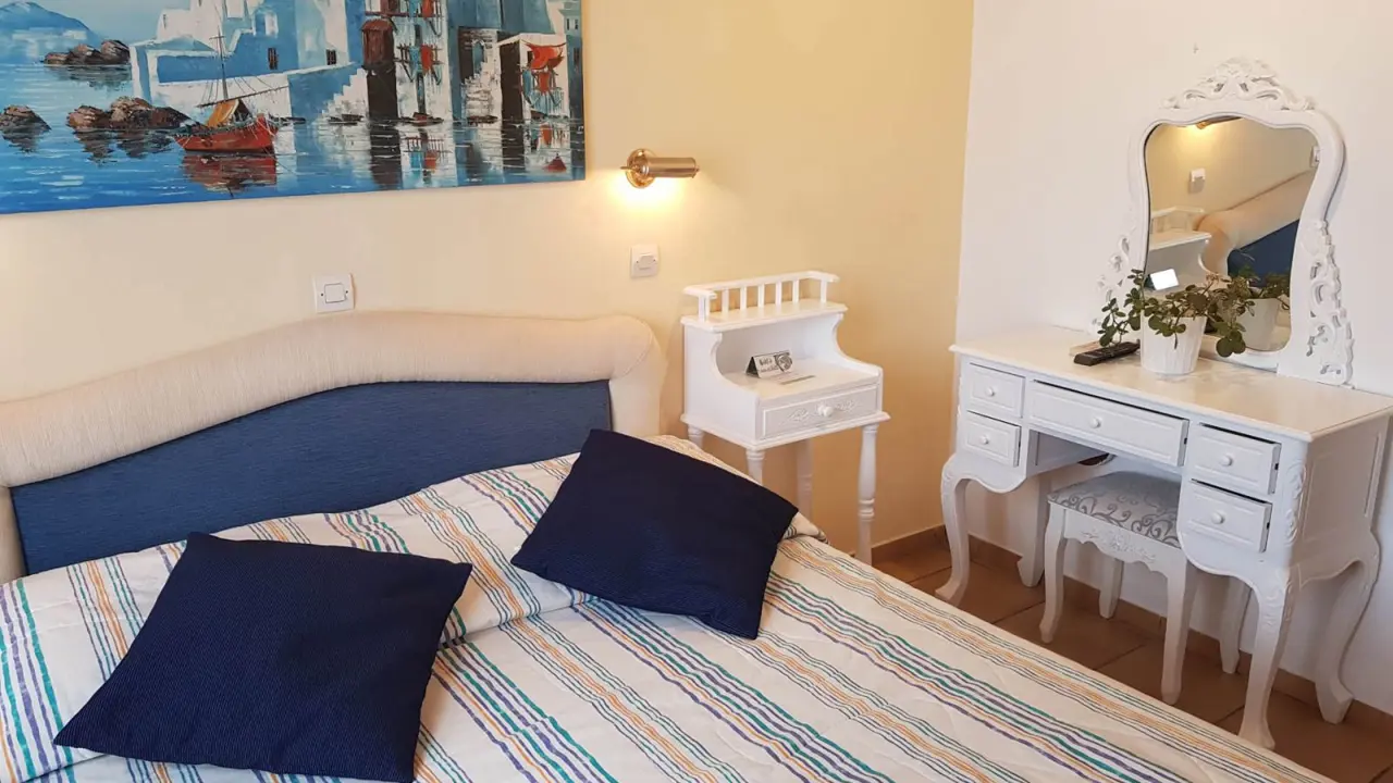 Bright double room at Hotel Ippokampos in Hydra, Greece, featuring a neatly made double bed, whitewashed walls, and traditional wooden furnishings