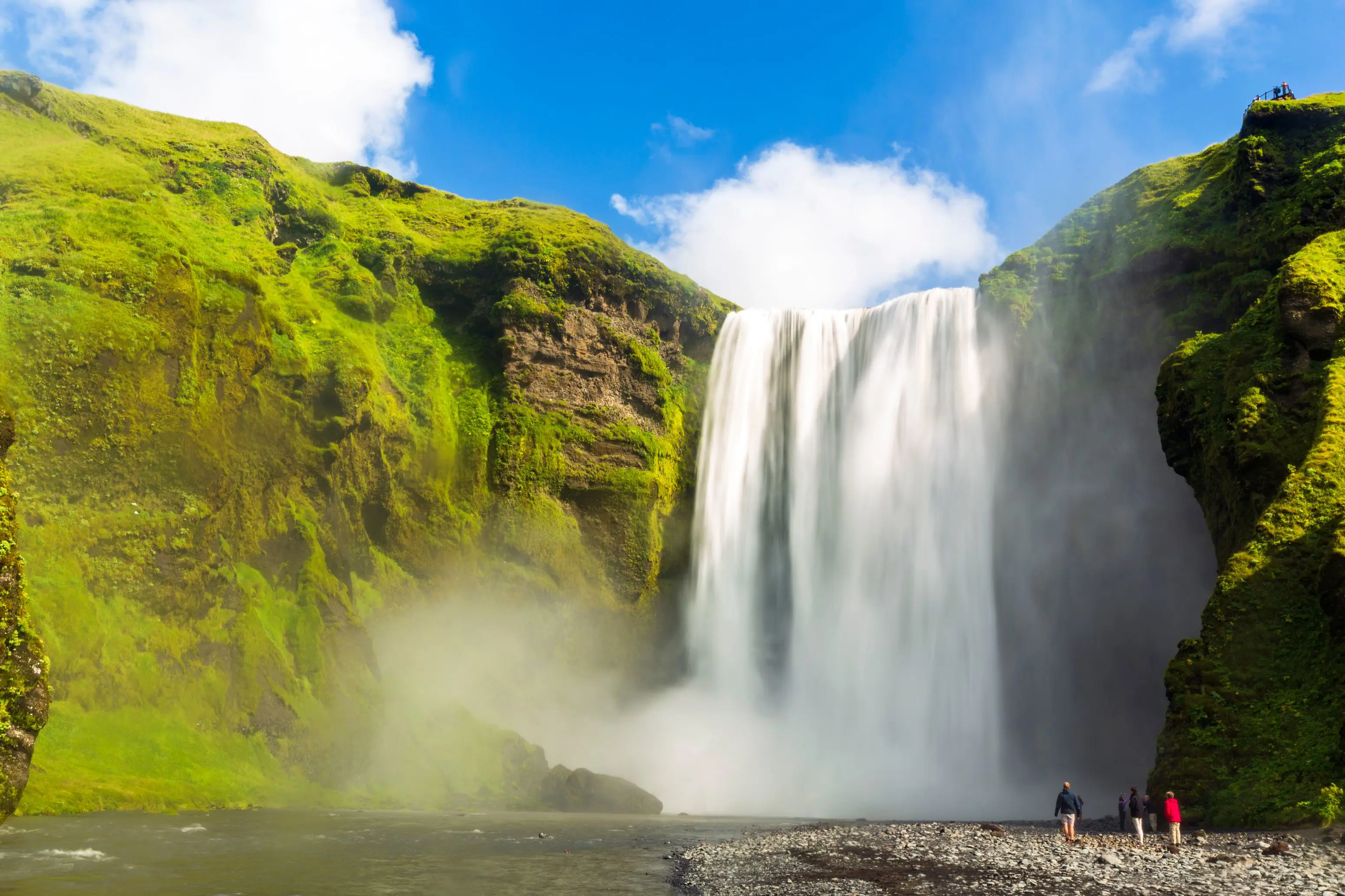 Waterfall surrounded by mossy rock. Steam coming off the water, people stood below the waterfall.