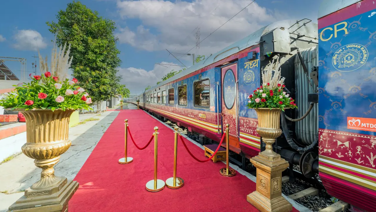 Exterior view of the Deccan Odyssey train at the platform, with a red carpet and gold barriers by the entrance