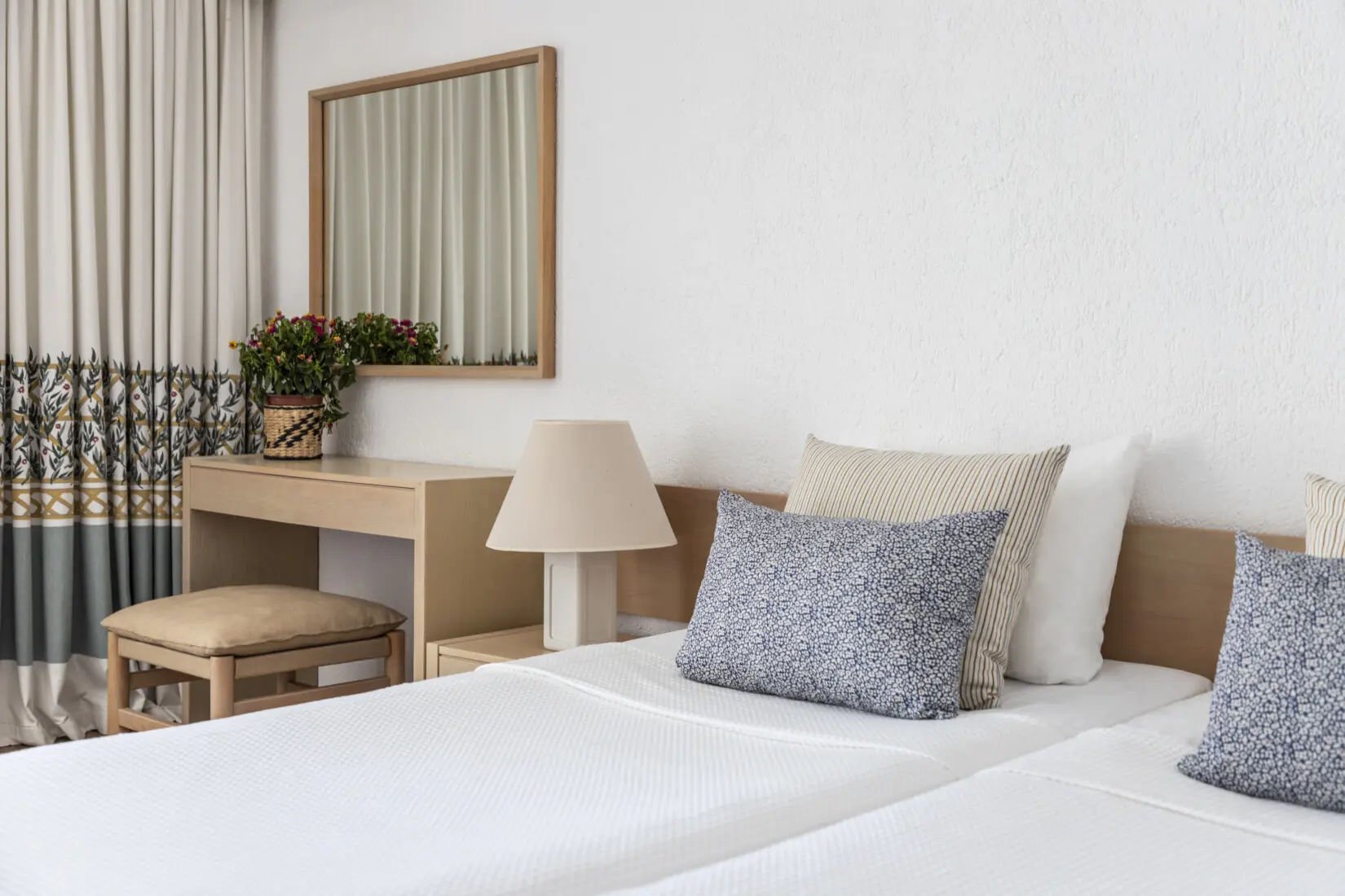 A twin room at Amalia Hotel, Olympia, featuring two twin beds with crisp white linens, wooden furnishings, and patterned curtains in neutral tones with dark green and gold accents