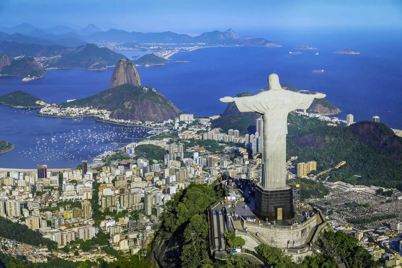 Panoramic view of Rio de Janeiro with Sugarloaf Mountain, the Christ the Redeemer statue, and city buildings along the coastline