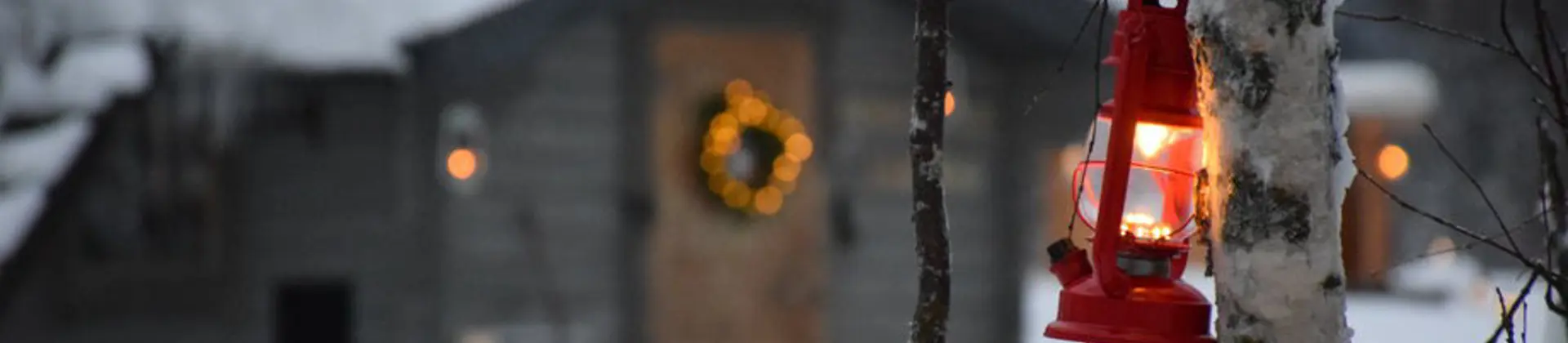 Close up of a lantern tied to a tree with Santa's Grotto in the background, in the snowy woods