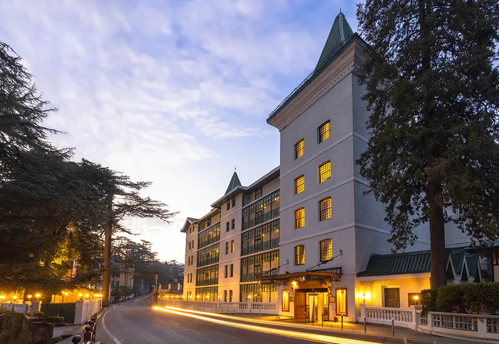The Oberoi Cecil in Shimla at dusk, warmly illuminated, highlighting the hotel’s historic architecture and landscaped surroundings