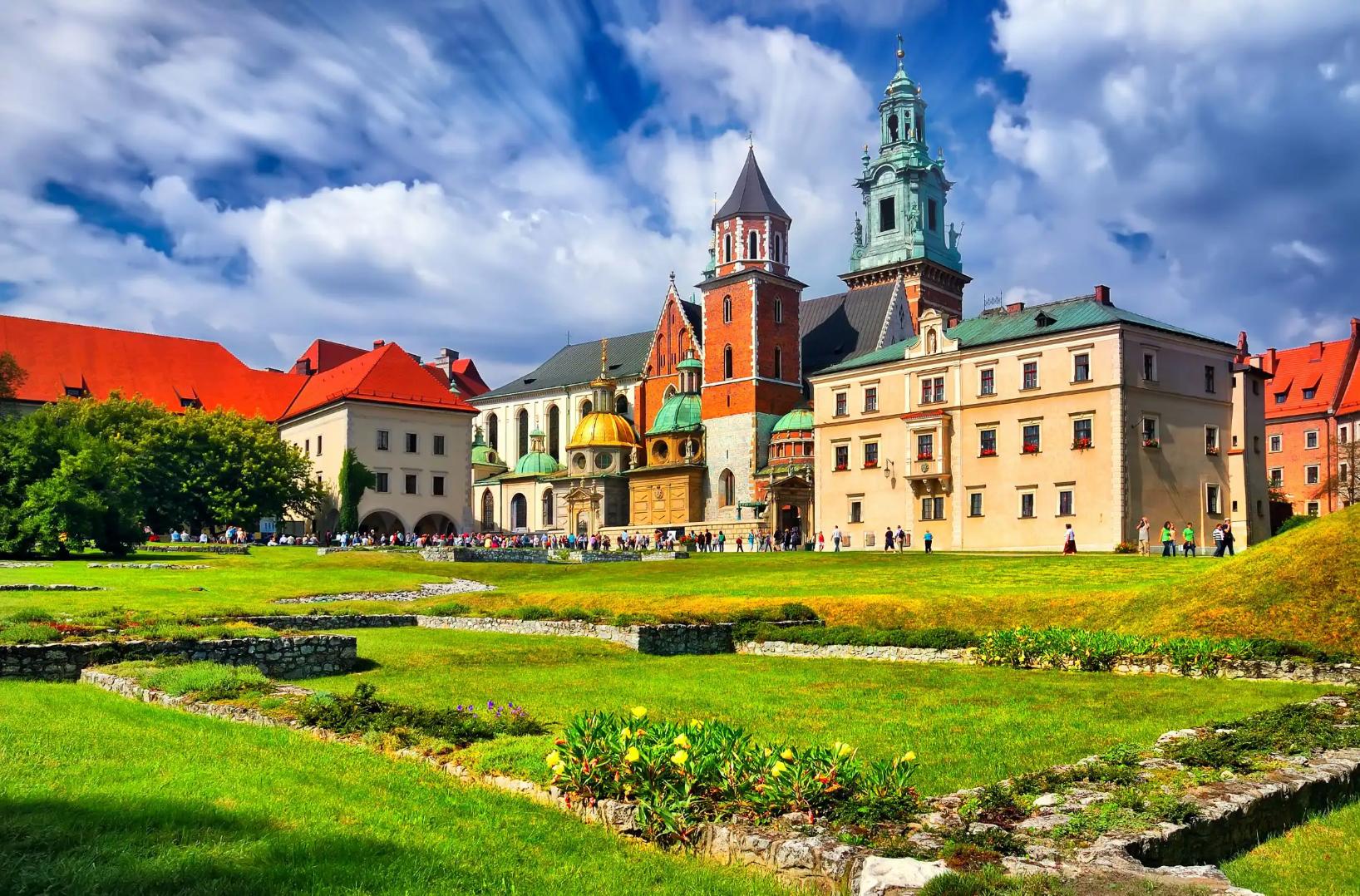 Wawel Castle in Kraków, Poland, showcasing its historic towers and red-brick walls beneath a cloudy blue sky