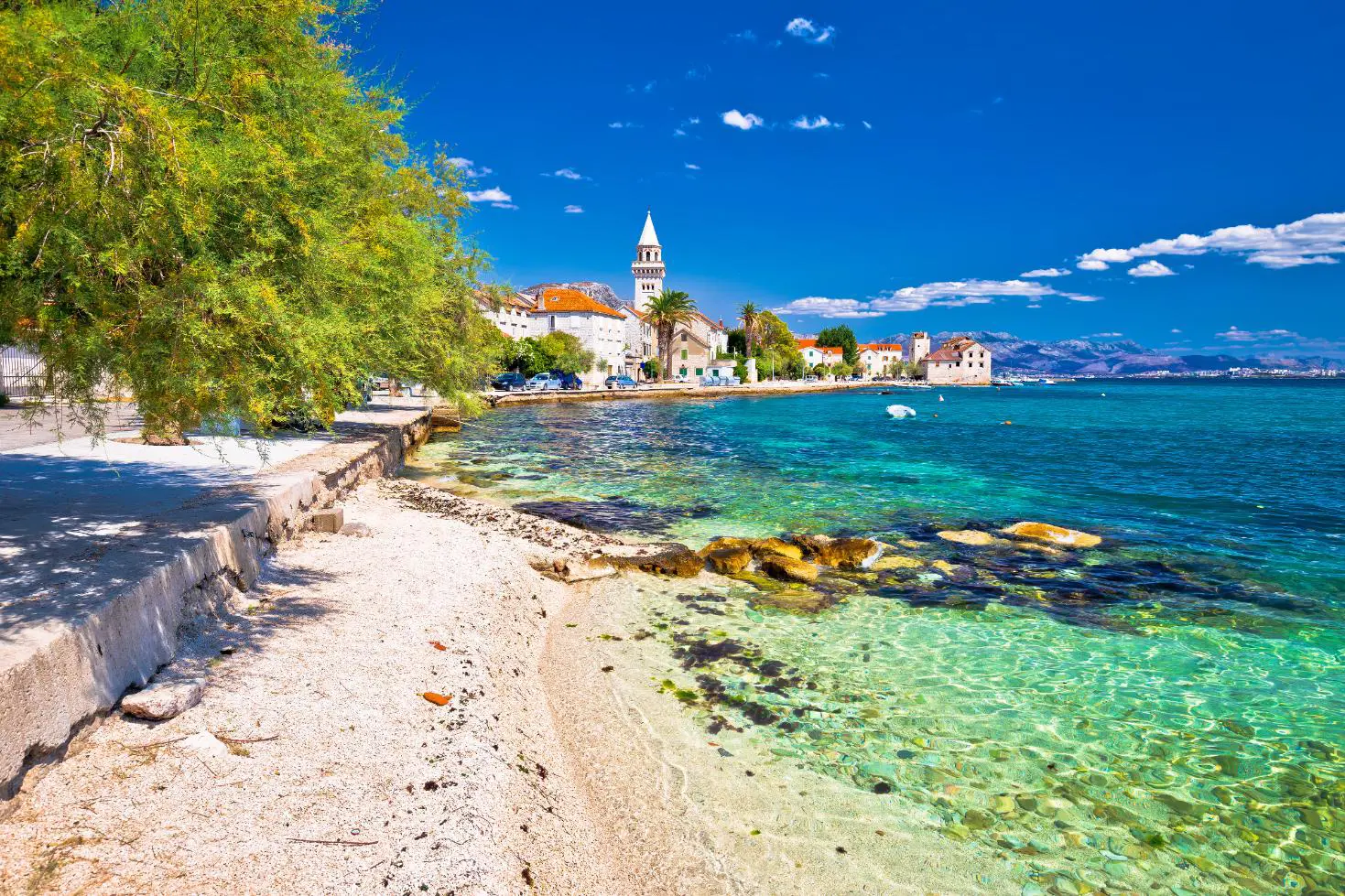 Scenic coastal view of Kaštel Štafilić near Split, Croatia, with crystal-clear turquoise water, stone buildings, and a church bell tower in the distance