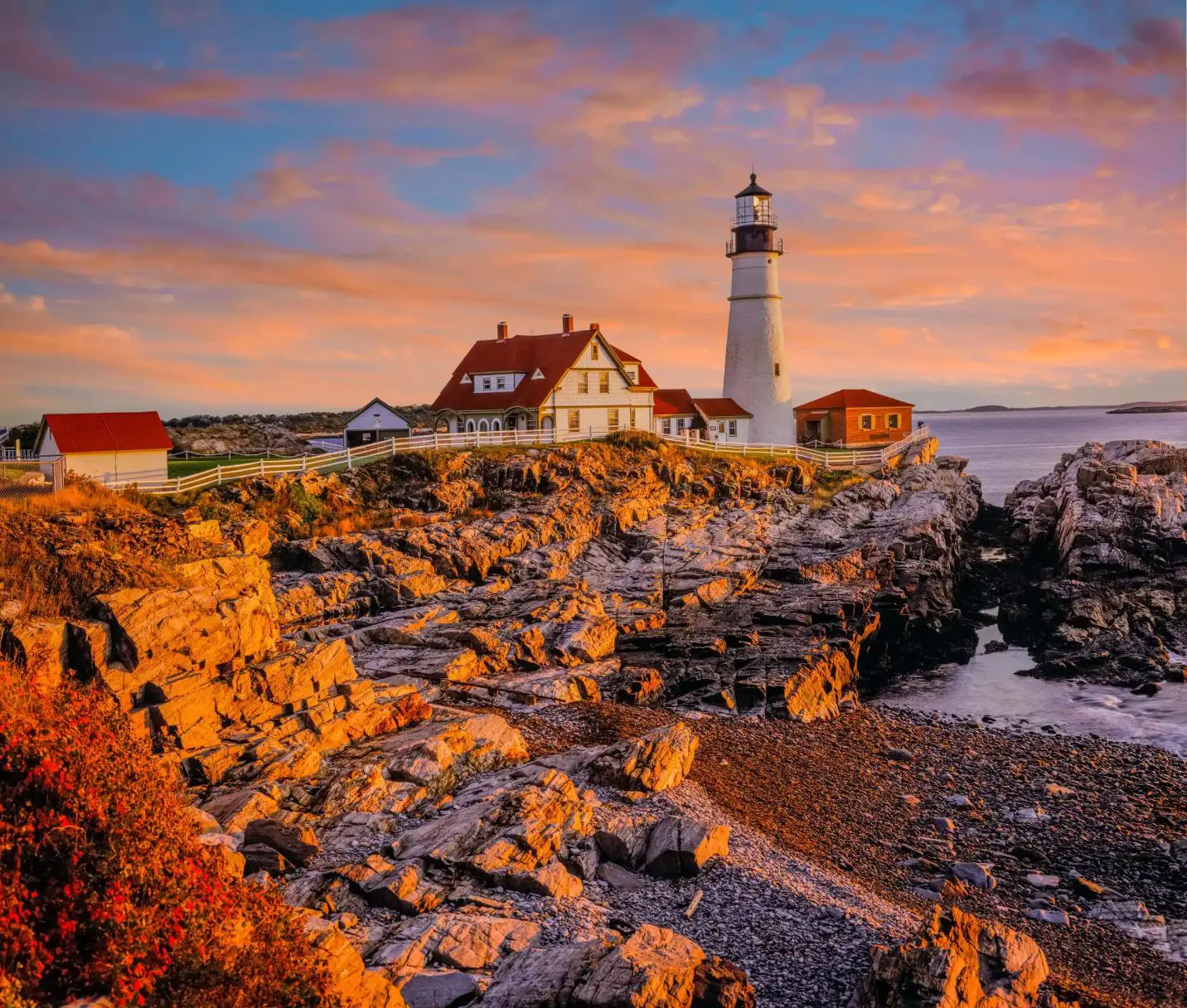Portland Head Lighthouse on the rocky Maine coast at sunset, with warm colours in the sky reflecting over the Atlantic Ocean
