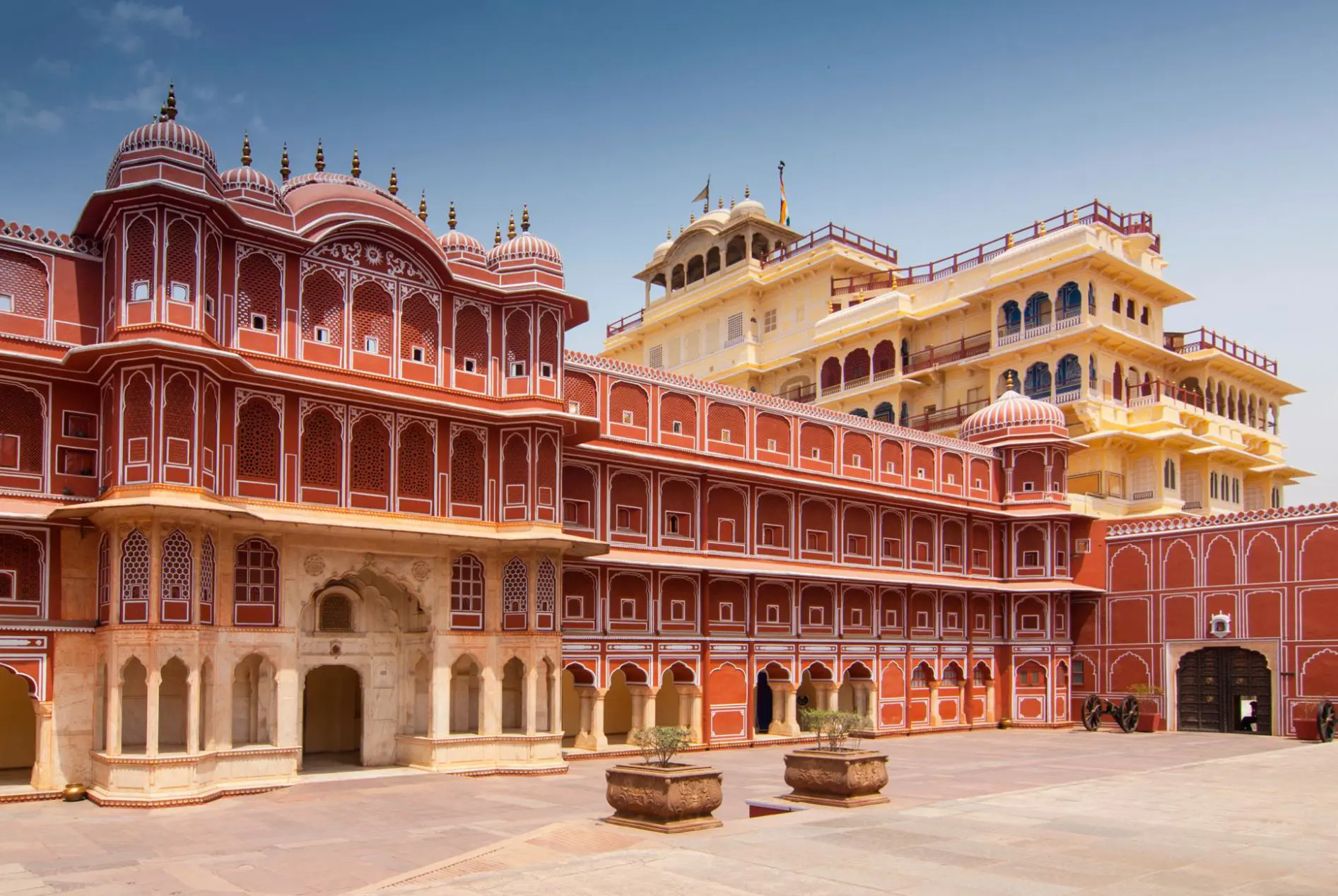 The ornate courtyard of the City Palace in Jaipur, displaying intricate red and white Rajasthani architecture with carved arches, domed roofs, and symmetrical windows