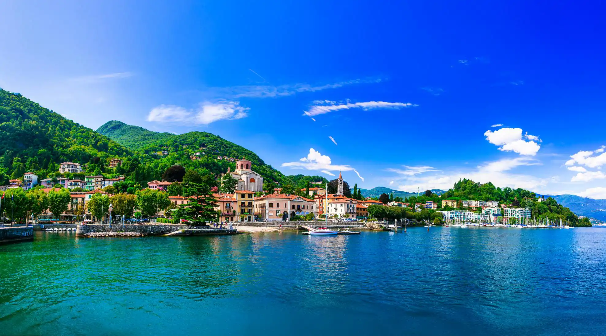 Lake Maggiore in Italy, with an Italian town on the shore beneath a bright, partly cloudy sky