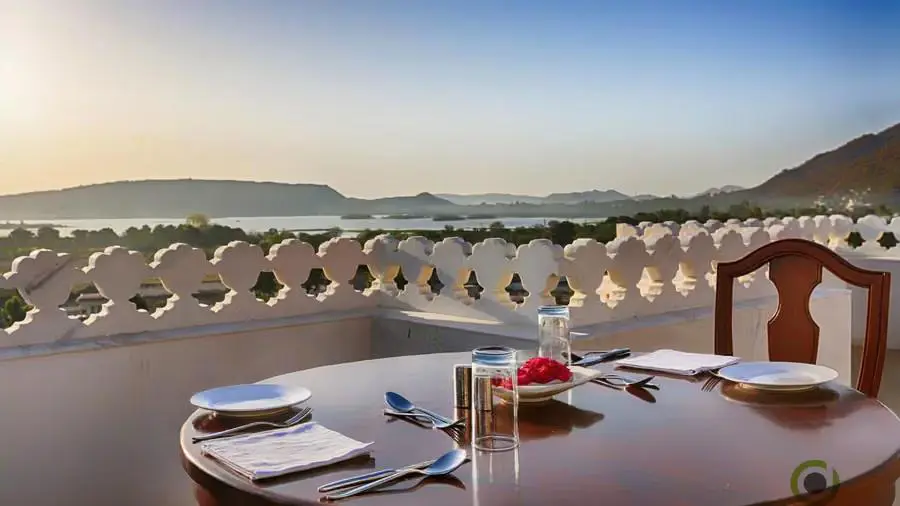 Outdoor dining table set for two on a terrace at Fateh Niwas Hotel, Udaipur, overlooking the lake and hills at sunset