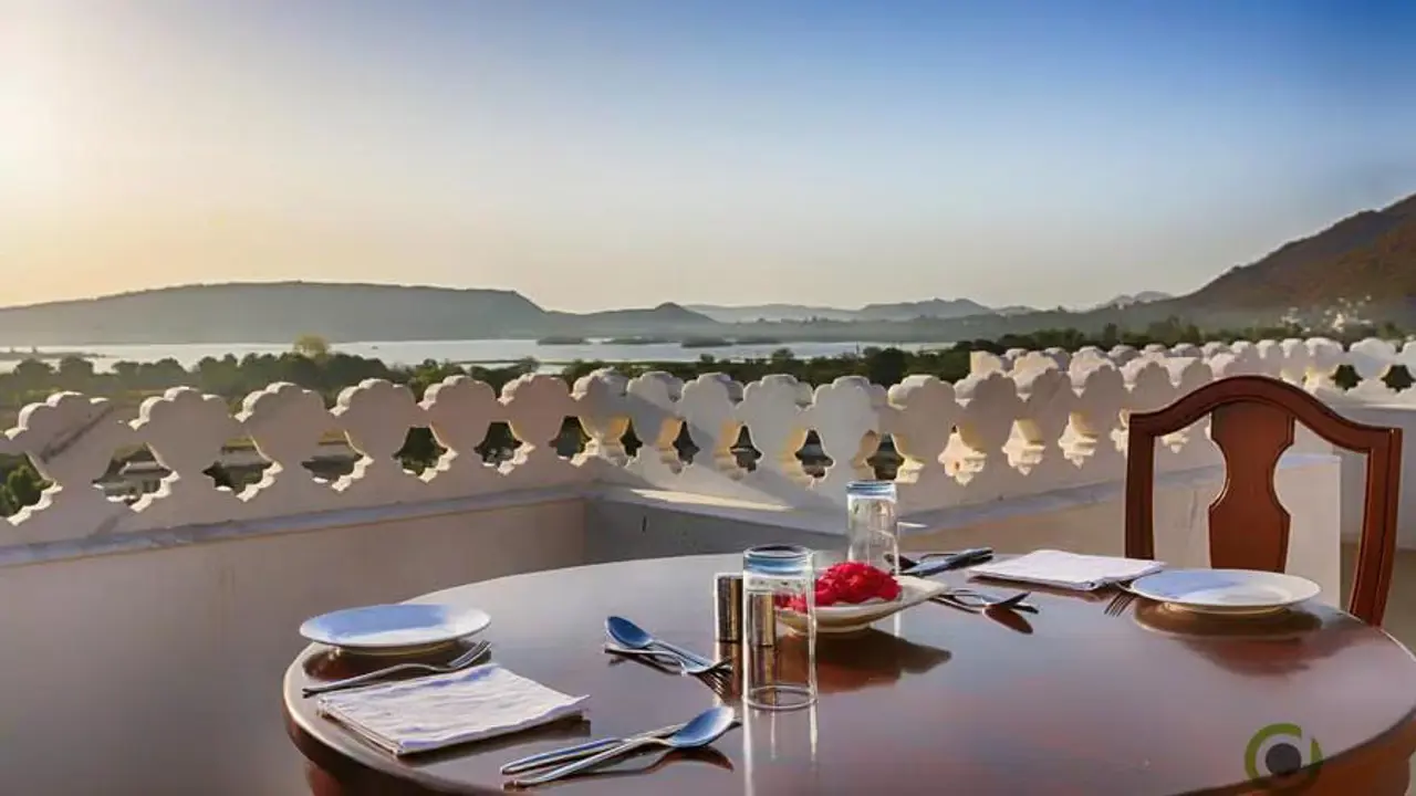 Outdoor dining table set for two on a terrace at Fateh Niwas Hotel, Udaipur, overlooking the lake and hills at sunset