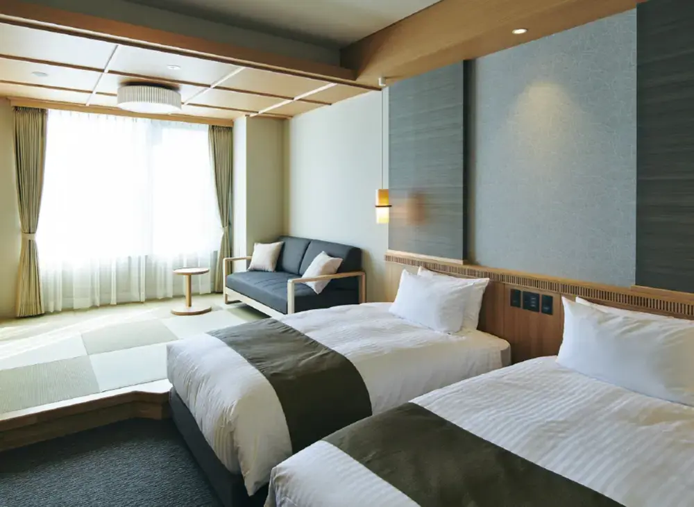 Bright and elegant twin bedroom in Hotel Kowakuen Haruka, with two beds, a sofa by the window, and a blend of modern and traditional Japanese design elements