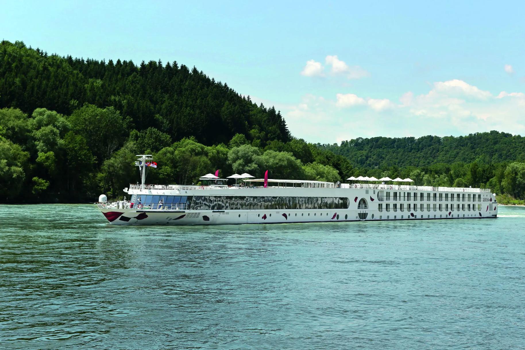 An A-ROSA river cruise ship sailing down a river with trees in the background