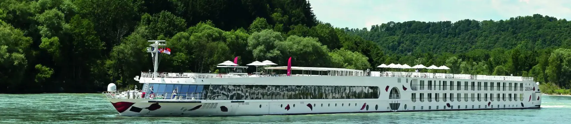 An A-ROSA river cruise ship sailing down a river with trees in the background