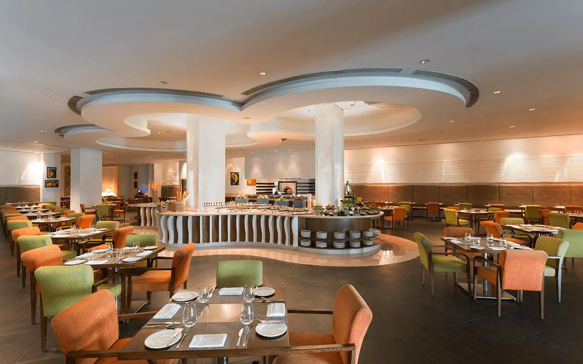 A spacious restaurant at WelcomHotel by ITC in Dwarka featuring colourful chairs, neatly set tables and a central buffet area