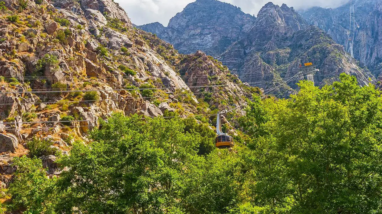 A yellow cable car from the Palm Springs Aerial Tramway in California ascending through a rocky mountain landscape with green trees below