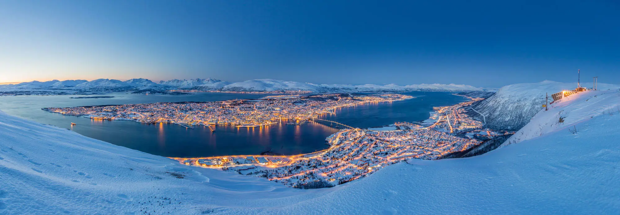 View of Tromso in the snow, at night time with light from the buildings lighting up the town