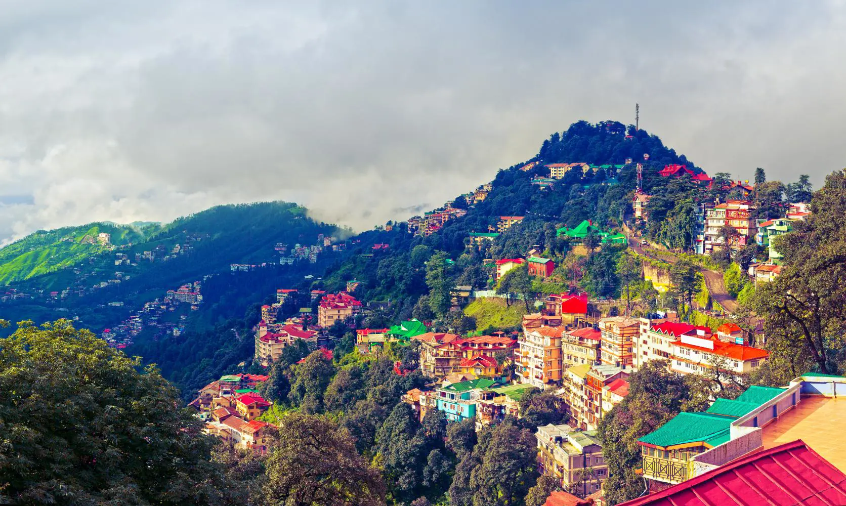 A panoramic view of Shimla’s colourful hillside buildings surrounded by green mountains and misty clouds in the Himalayan foothills