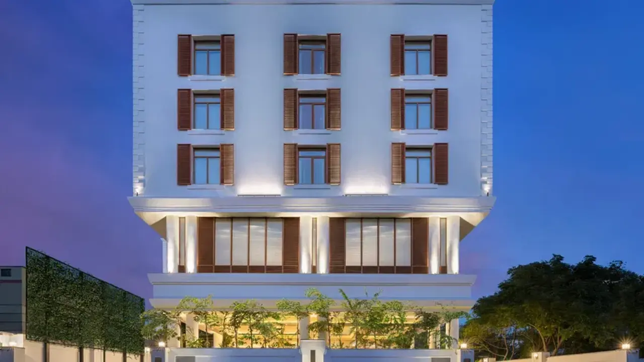 Modern exterior of The Residency Towers hotel in Pondicherry, featuring white paintwork and brown shutters, surrounded by trees at night