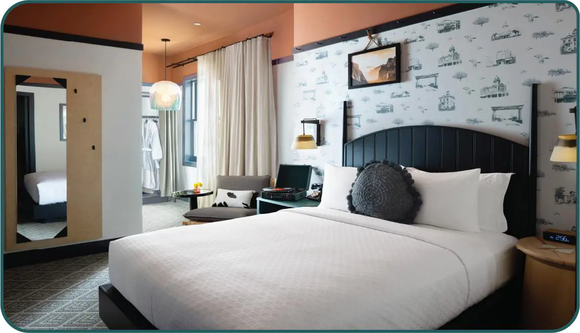 Stylish bedroom at the El Capitan Hotel, Merced, featuring a black wooden bed, patterned wallpaper behind, and orange-painted upper walls and ceiling, with warm lighting creating a cosy atmosphere