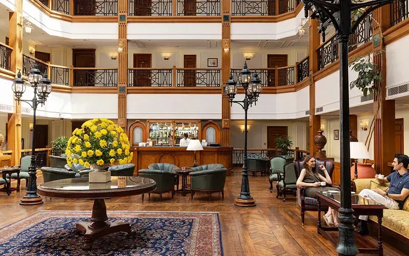 Lounge area of the Oberoi Cecil, Shimla, with tiered rooms surrounding the space, comfortable seating, wooden floors, and yellow flowers on the central table