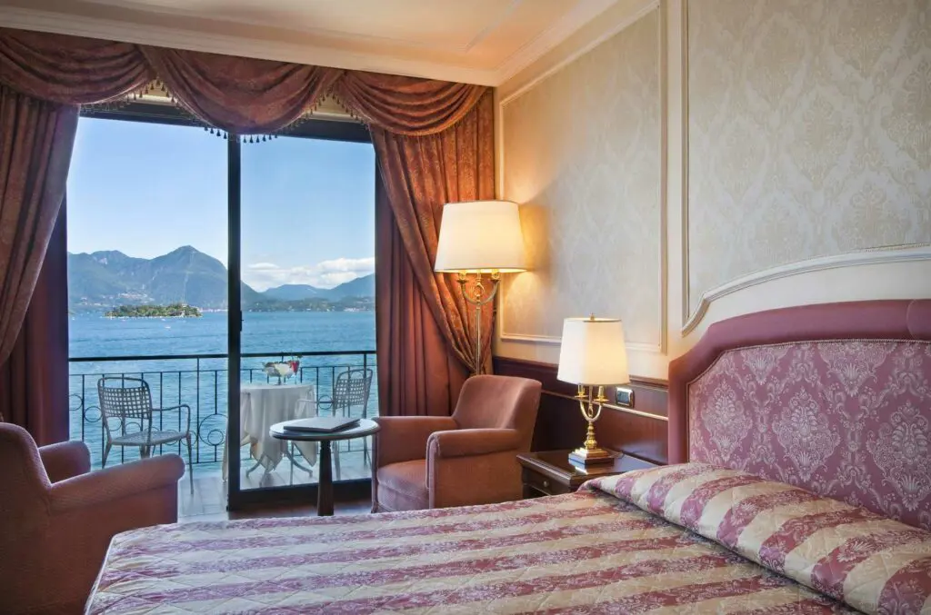 Elegant bedroom at Grand Hotel Dino in Baveno with striped bedding and two lounge chairs by the window overlooking the lake and mountain views