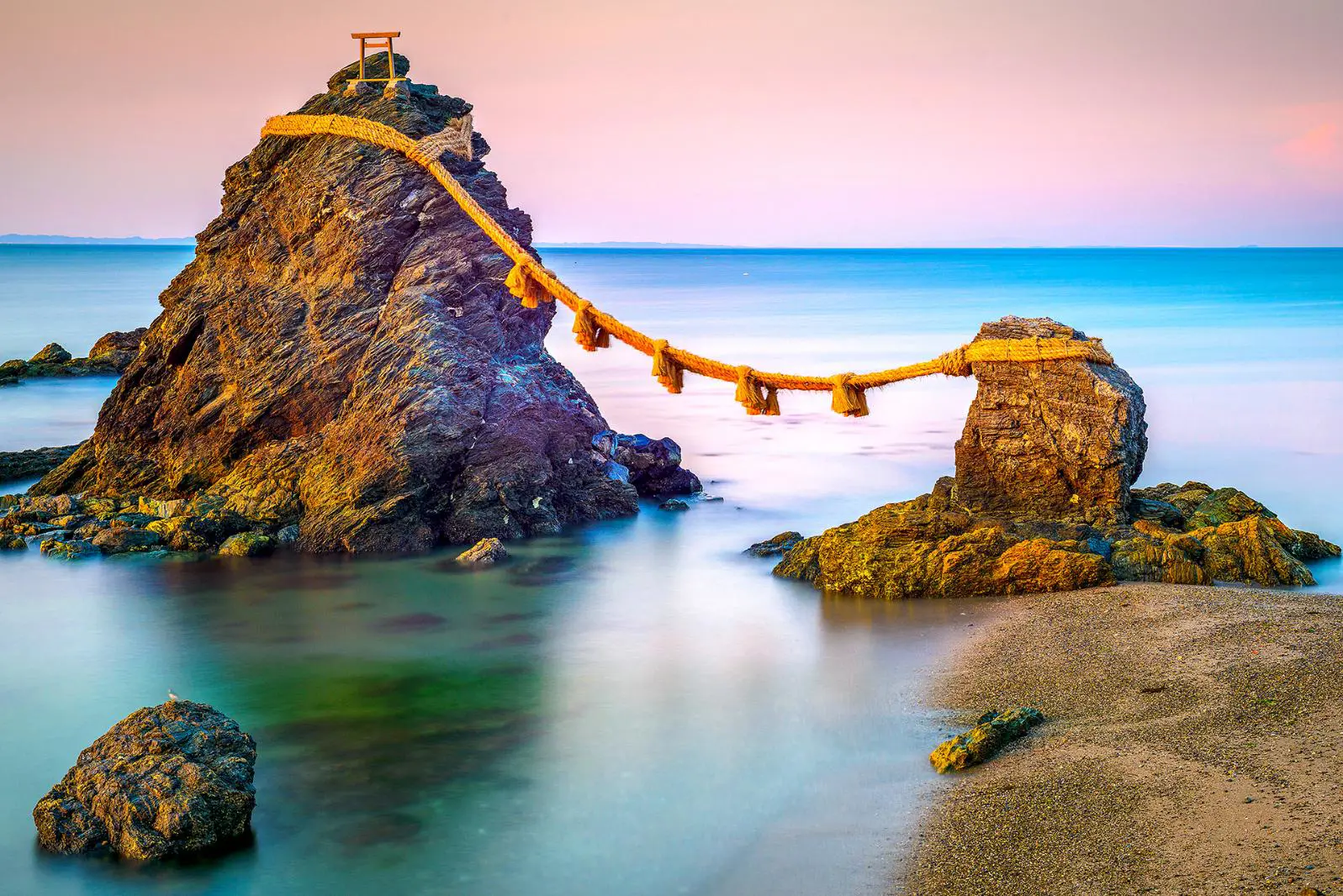 The Meoto Iwa Rocks, connected by a sacred rope in the sea at sunrise near Ise, Japan, with a small torii gate atop the larger rock