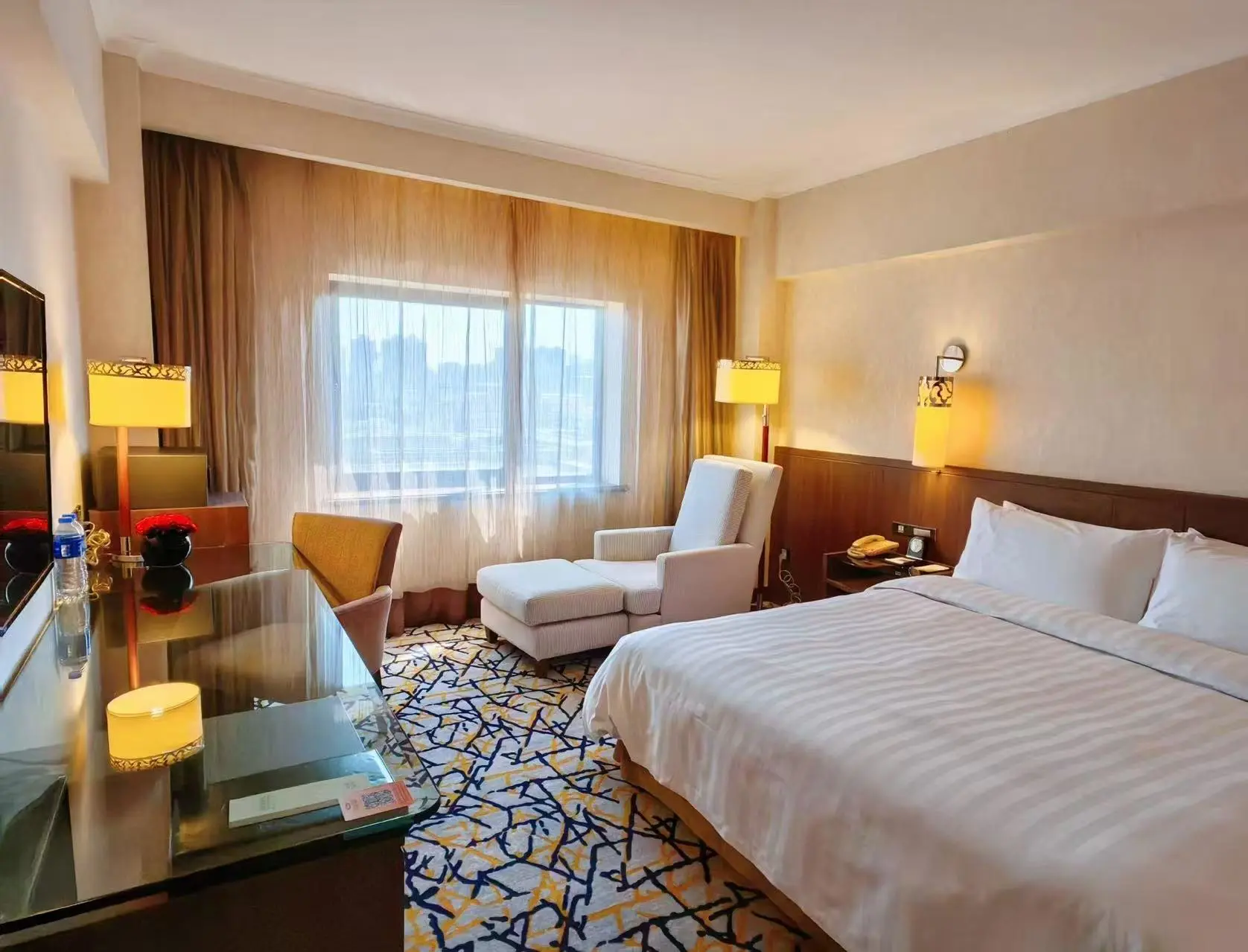 Comfortable hotel room featuring cosy décor, a large bed, desk and an armchair near a window at the Grand Noble Hotel Xi’an in Xi’an, China