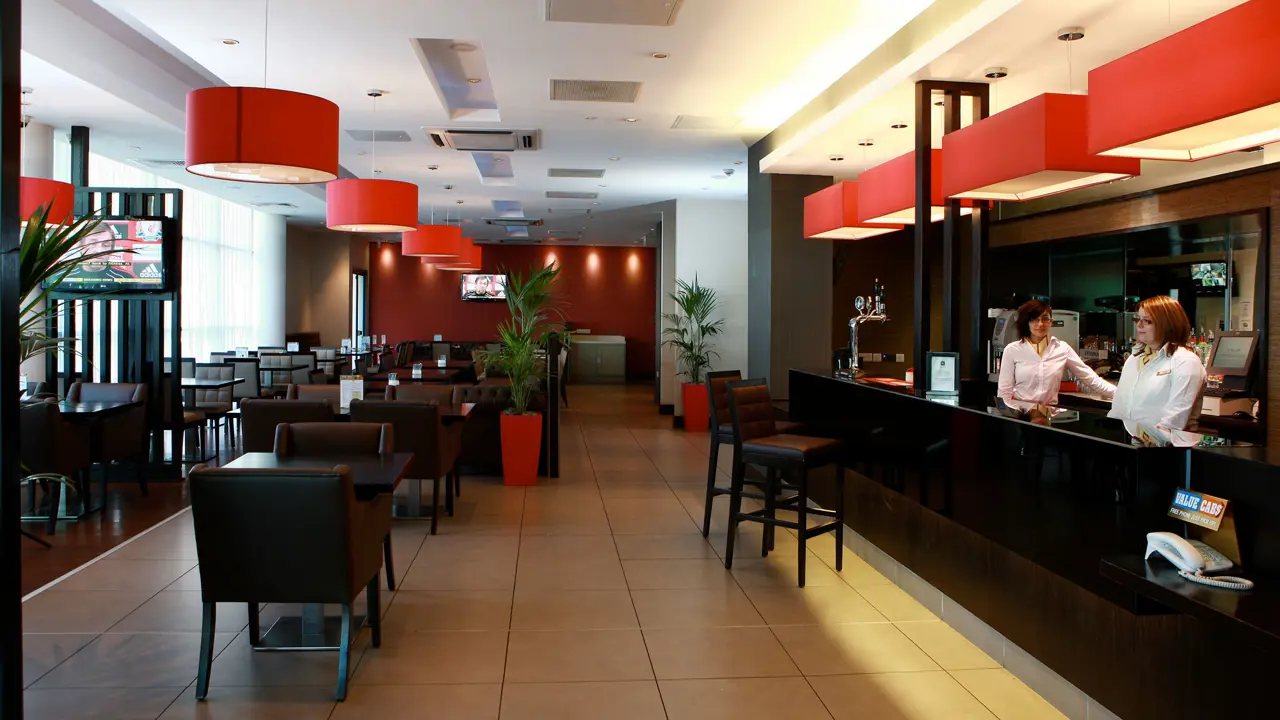 Modern bar and reception area at the Ibis Belfast City Centre, featuring red lighting, comfortable seating, and a contemporary design