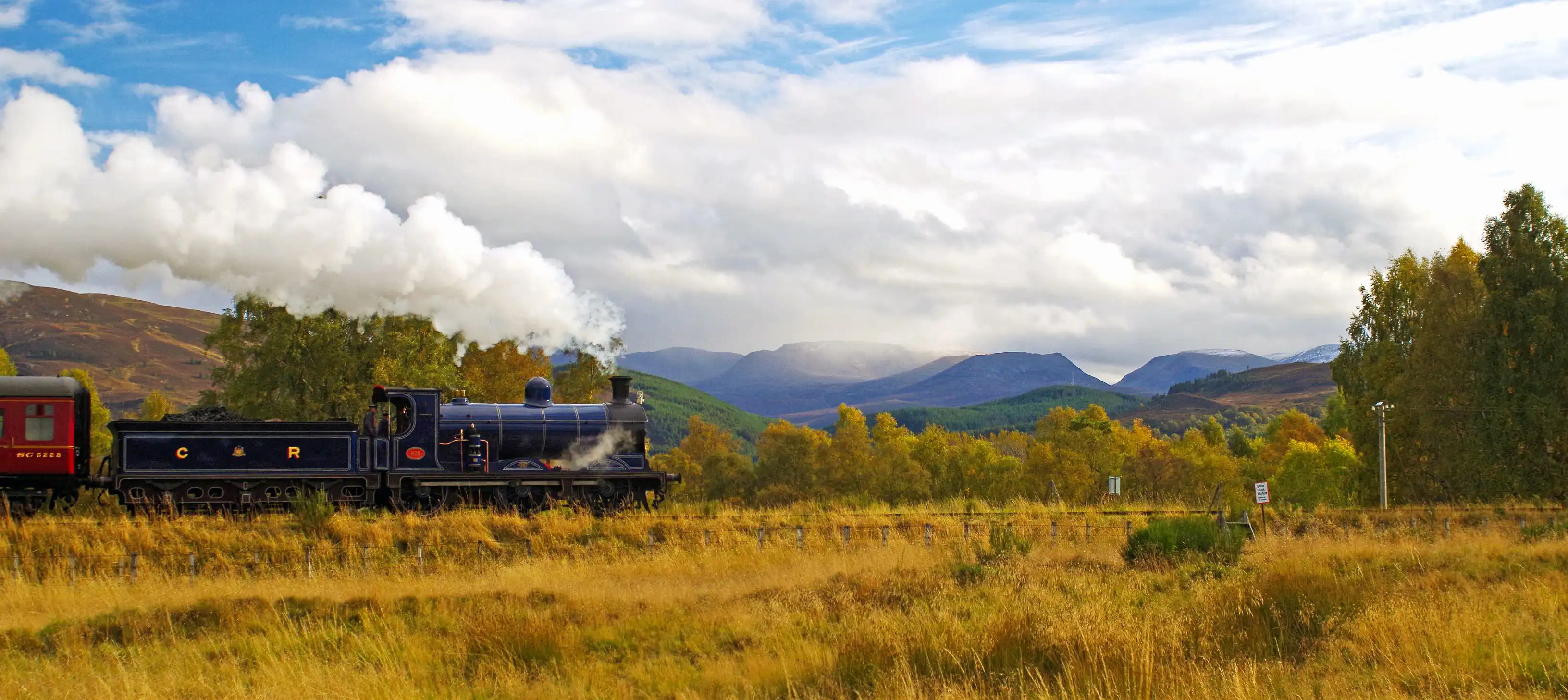 Steam train approaches Kinchurdy Bridge against Cairngorms 