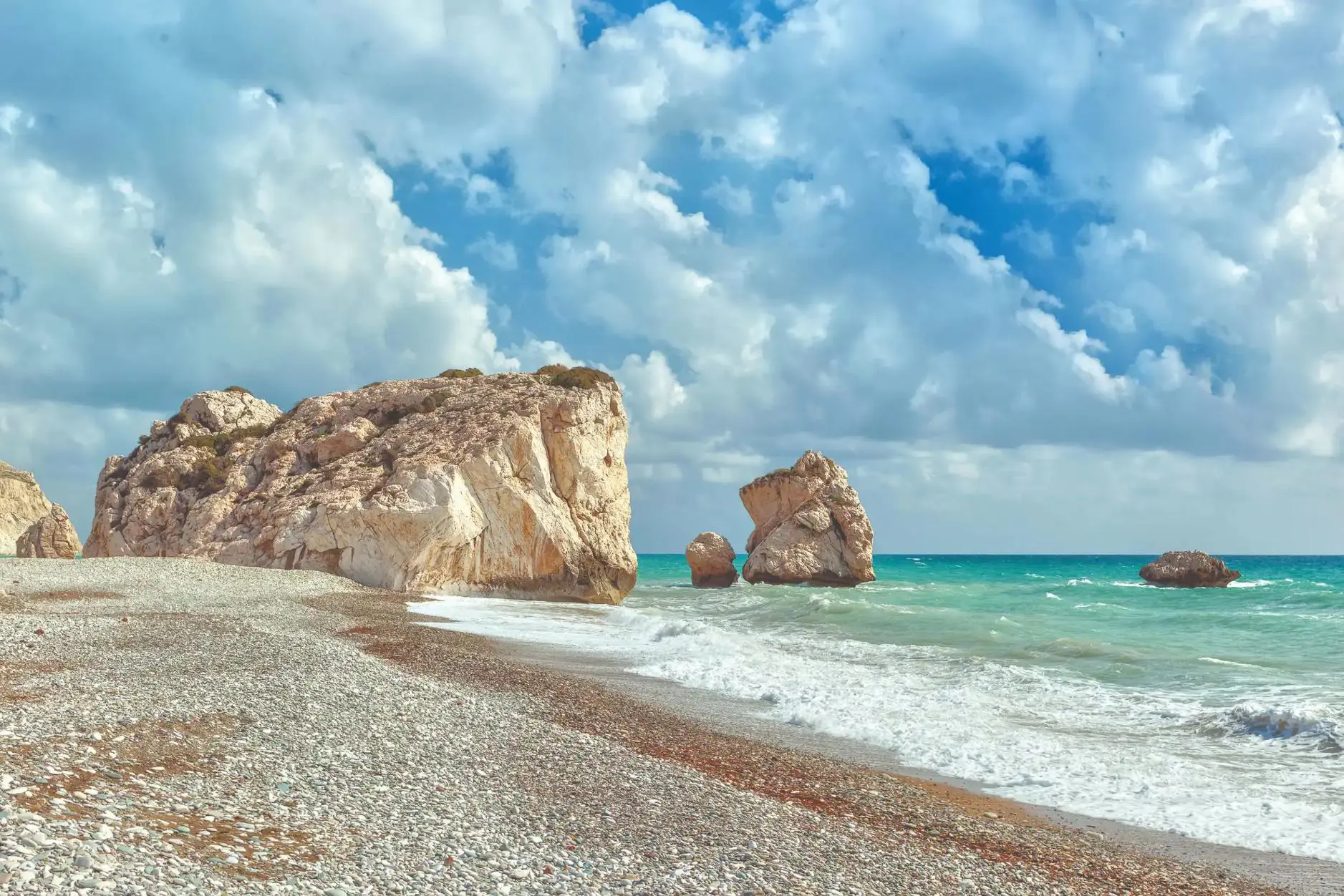 A cloudy day with waves crashing on a pebbled beach near Aphrodite’s Rock in Cyprus