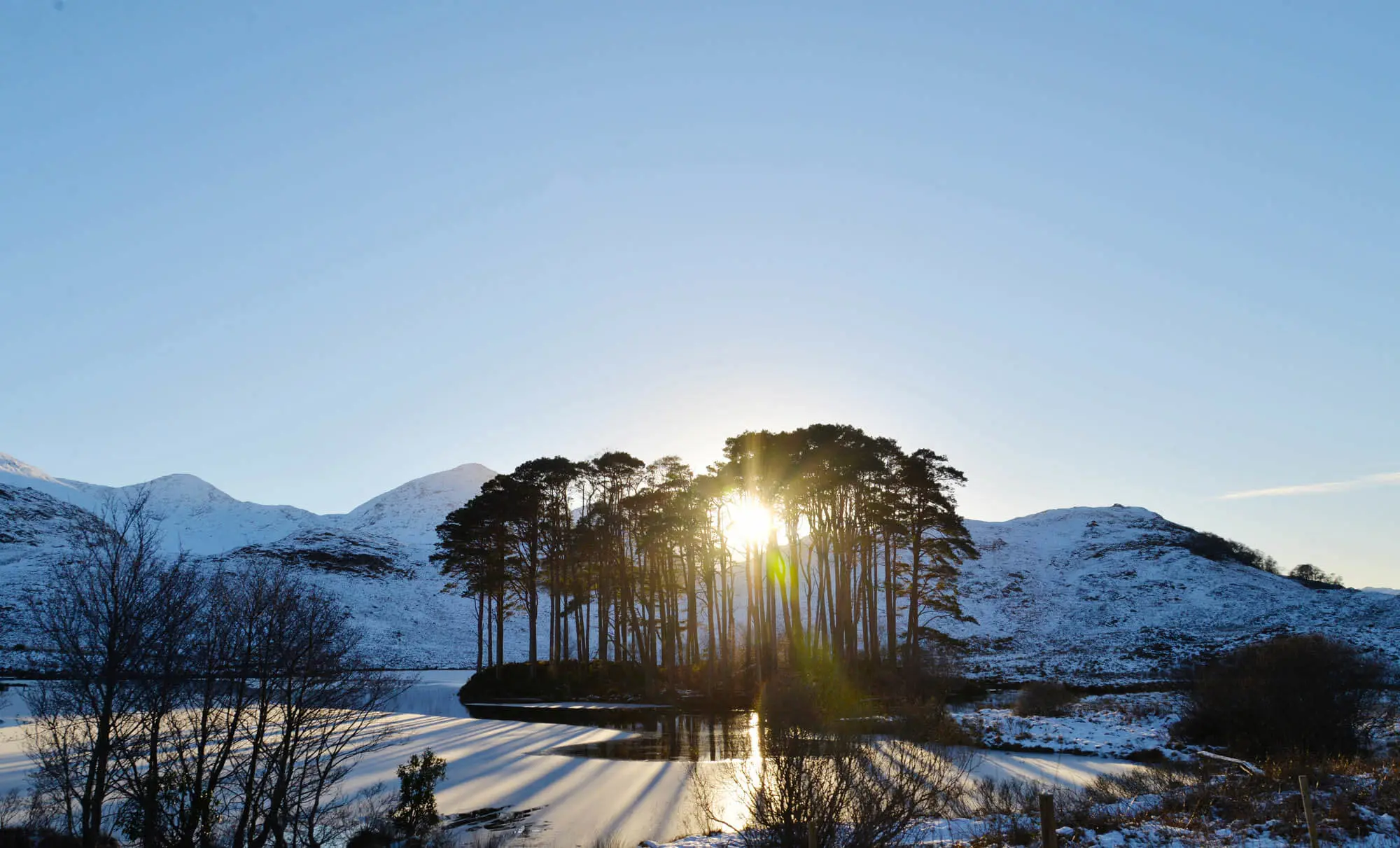 View of the Scottish Highlands in the snow, with the sun coming through the trees 