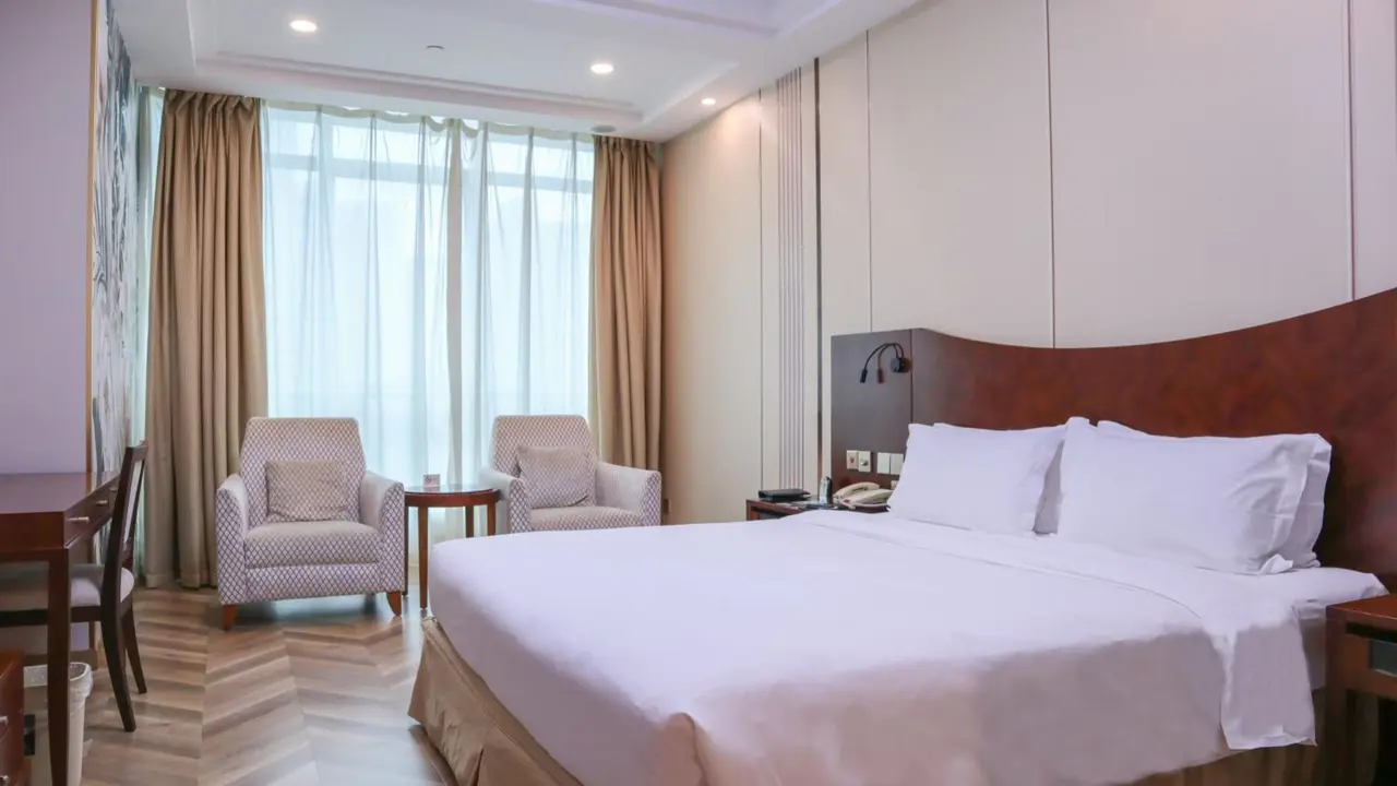 Bright hotel room with a large bed, armchairs and floor-to-ceiling curtains at the Shanghai Metropark Jichen Hotel in Shanghai, China